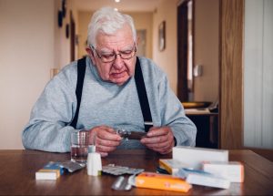 elderly-man-looking-at-his-prescription-medications-in-his-home-at-a-table