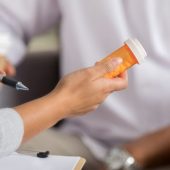 female-pharmacist-holding-a-medication-bottle-and-talking-with-a-male-patient