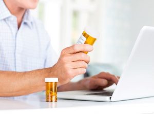 man-holding-prescription-pill-bottle-in-front-of-a-laptop